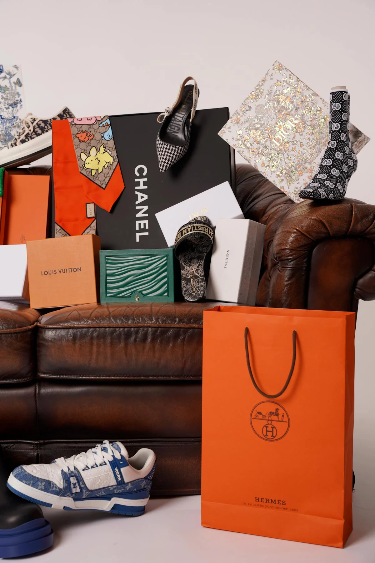 Luxury pieces from Chanel, Hermès, Dior and Louis Vuitton arranged on a leather sofa
