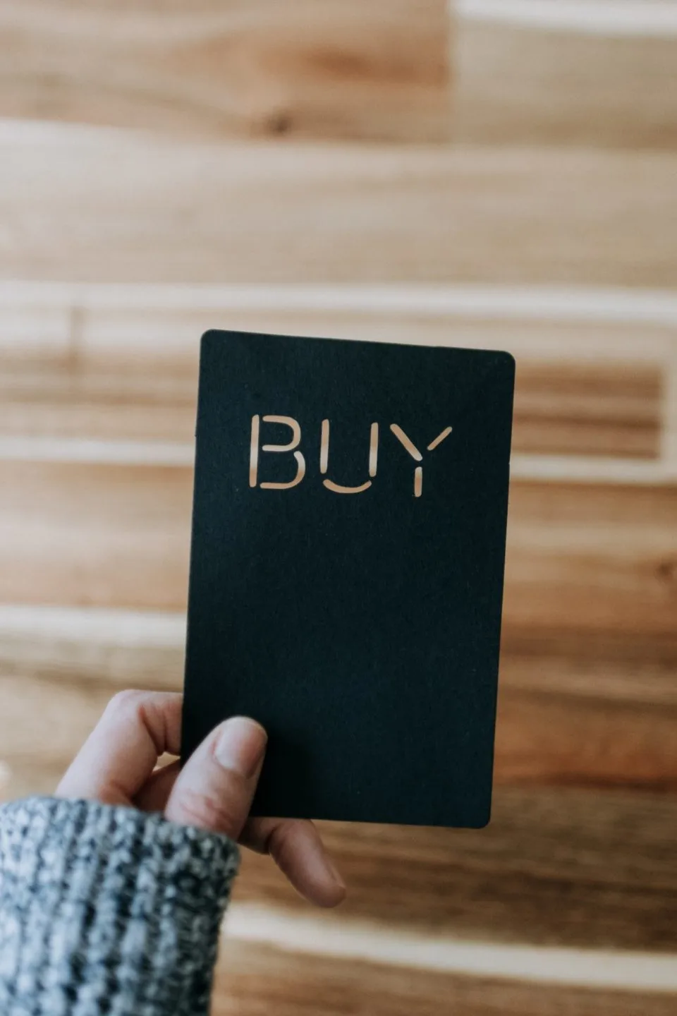 A hand holding a black card reading BUY