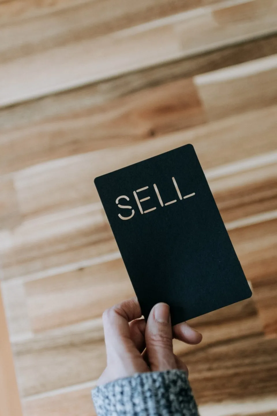 A hand holding a black card reading SELL